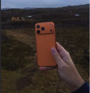 An orange iPhone held up against a hillside